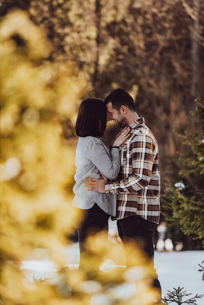 Beautiful couple hugging between snowy pines woman in casual clothes holding hands on man chest Selective focus