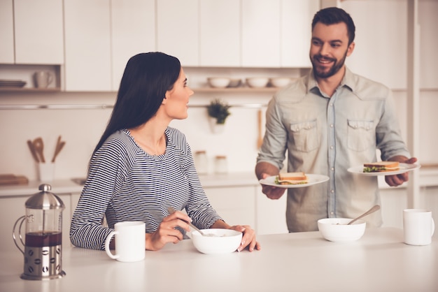 Beautiful couple is eating sandwiches, talking and smiling.