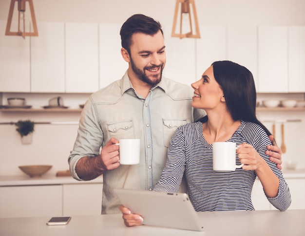 beautiful couple is using a digital tablet, holding cups.
