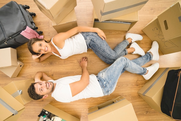 The beautiful couple lay on the floor near carton boxes. view from above