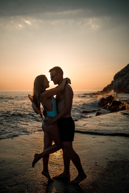 Beautiful couple in love on the background of the sunset by the sea. Young woman and man hugging by the sea at sunset