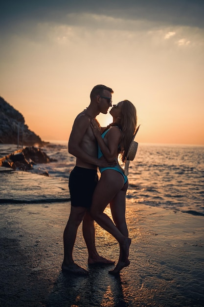 Beautiful couple in love on the background of the sunset by the sea Young woman and man hugging by the sea at sunset