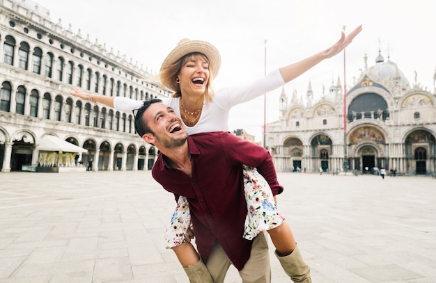 Bella coppia innamorata divertirsi abbracciando e ridendo facendo cavalluccio in vacanza a venezia, italia in piazza san marco.