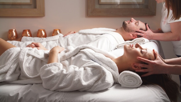 Photo beautiful couple lying down on massage beds enjoying a head massage in luxury spa.