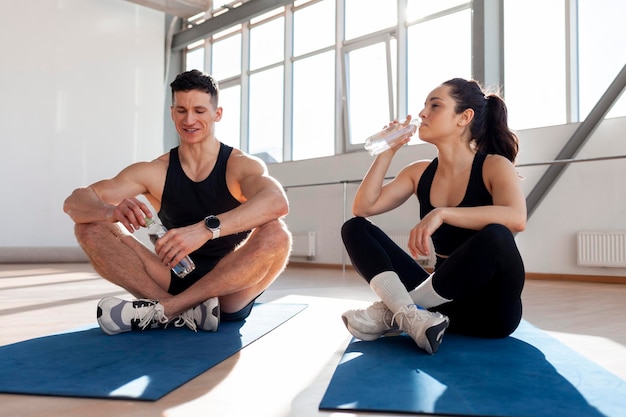 Beautiful couple in sportswear sitting on yoga mats in the gym and smiling athletic man and woman