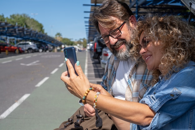 Beautiful couple of tourists in the parking of the airport looking at smart phone