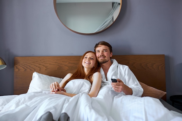 Beautiful couple watch tv on bed, have rest in hotel at weekends