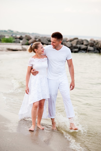 Beautiful couple in white clothes walking on the sea