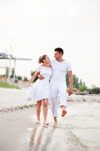 Beautiful couple in white clothes walking on the sea