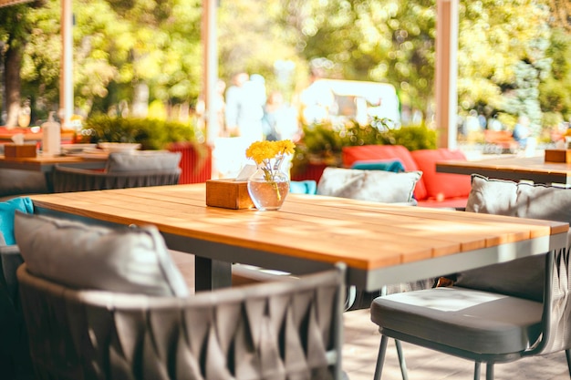 Beautiful cozy cafe terrace with wooden table, chair and yellow flowers in a glass vase in summer