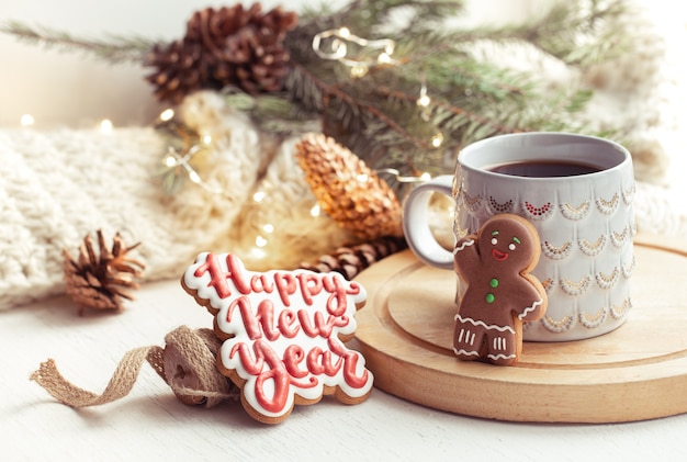 Beautiful cup with handmade gingerbread cookies covered with glaze close up on a cozy blurred background with lights.