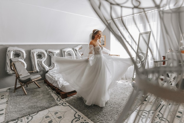 Photo beautiful curly brownhaired bride in a white dress poses for a photographer circling the room in a beautiful dress with sleeves wedding photography closeup portrait chic hairstyle