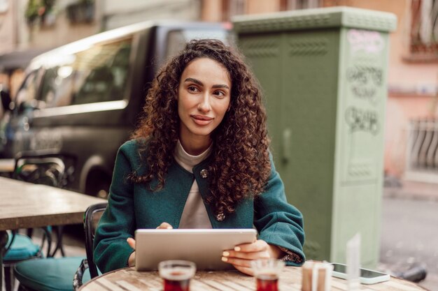 Beautiful curly businesswoman using digital tablet outdoors in cafe close up