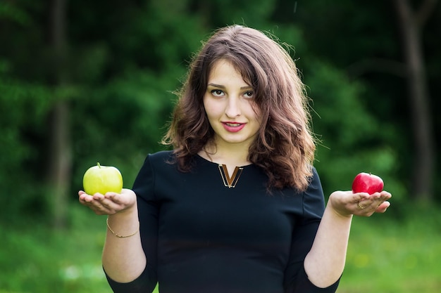 Beautiful curly girl in a black dress holding a green apple in the forest