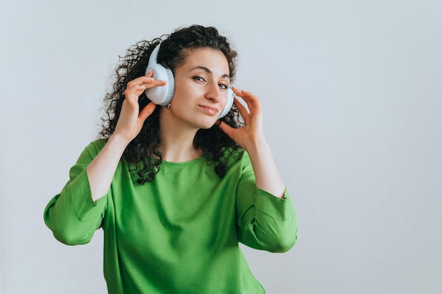 Beautiful curly hispanic young adult woman in headphones and green blouse enjoying music