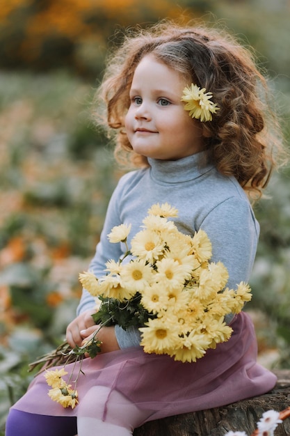 beautiful curly little girl in blue shirt in park with flowers at fall time autumn health card