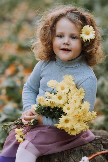 beautiful curly little girl in blue shirt in park with flowers at fall time autumn health card