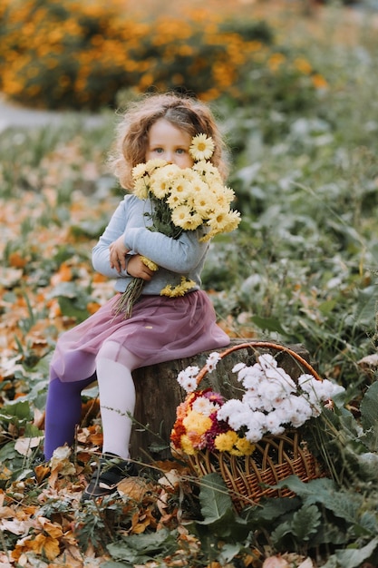 beautiful curly little girl in blue shirt in park with flowers at fall time autumn health card