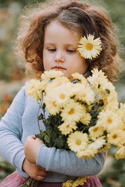 beautiful curly little girl in blue shirt in park with flowers at fall time autumn health card