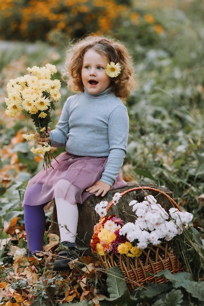 Bella bambina riccia in camicia blu nel parco con fiori in autunno tessera sanitaria autunnale
