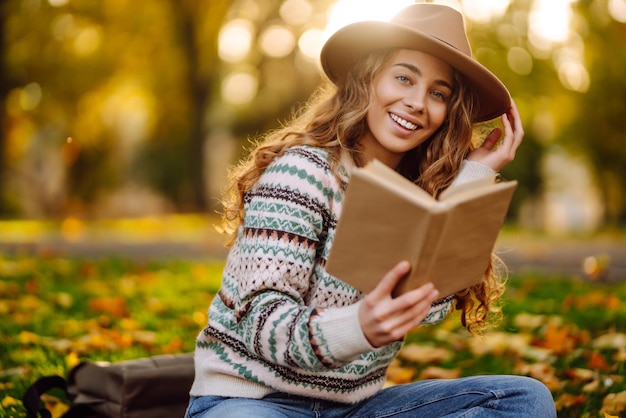 Photo beautiful curly woman in hat on mat with book in autumn park relaxation solitude with nature