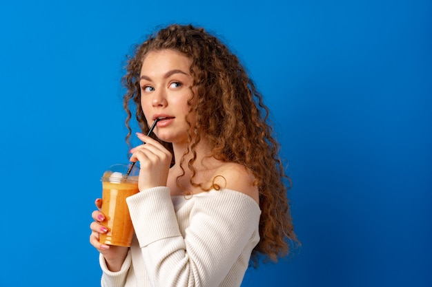 Bella donna dai capelli ricci che beve succo d'arancia su sfondo blu