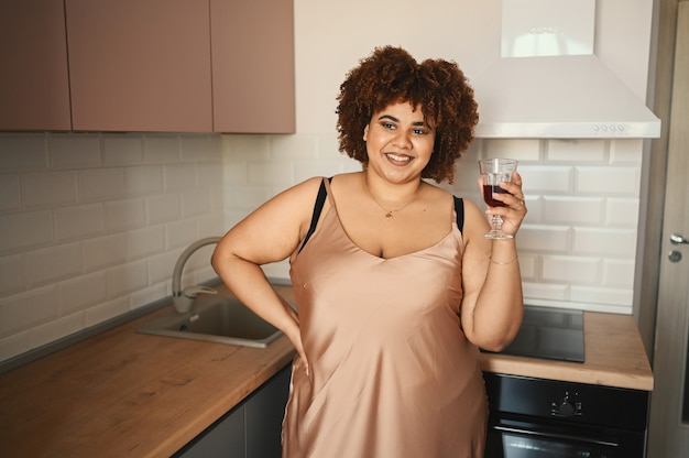 Beautiful curvy plus size african black woman afro hair drinking red wine on modern scandinavian