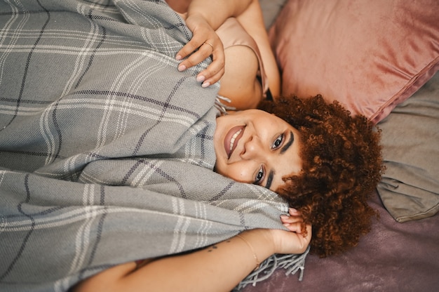 Beautiful curvy plus size african black woman afro hair lying on bed with grey plaid blanket cozy