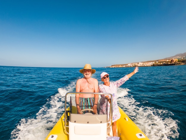 Beautiful and cute couple of seniors or old people in the middle of the sea driving and discovering new places with small boat. Mature woman holding a phone and taking a selfie with hew husband