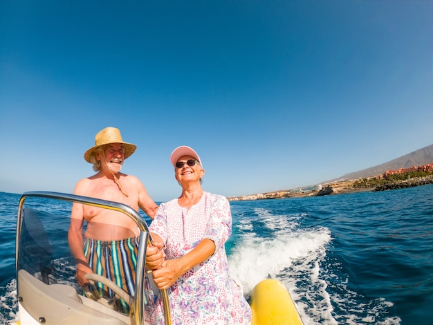 Beautiful and cute couple of seniors or old people in the middle of the sea driving and discovering new places with small boat. Mature woman holding a phone and taking a selfie with hew husband