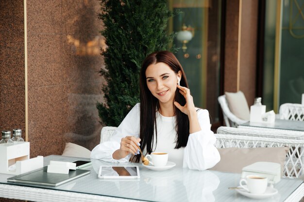 A beautiful cute girl in a cafe drinks coffee at a table.