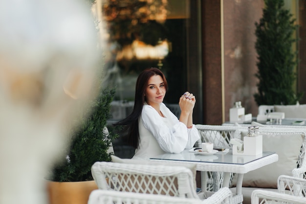 Красивая милая девушка в кафе пьет кофе за столиком.