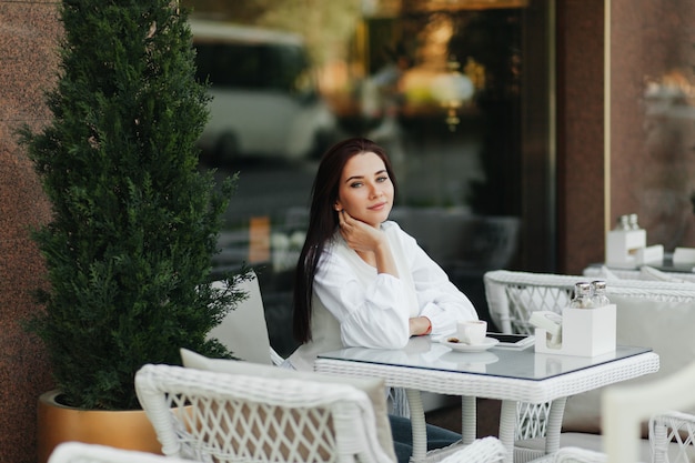 A beautiful cute girl in a cafe drinks coffee at a table.