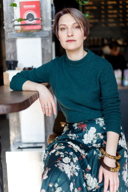 Beautiful cute girl in the cafe looking at the camera with coffee smiling. Green knitted sweater. fashionably dressed girl. girl looks at the phone. business lady