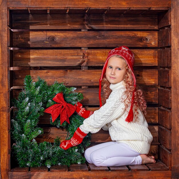 Beautiful cute girl child in a wooden square location in Christmas decorations