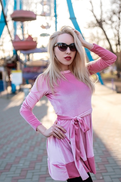 La bella ragazza carina con un vestito rosa sta camminando nel parco divertimenti