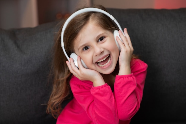 La bella bambina felice sveglia ascolta musica sulle cuffie senza fili. divertente bambina ballare, cantare e passare al ritmo. bambino che indossa le cuffie.