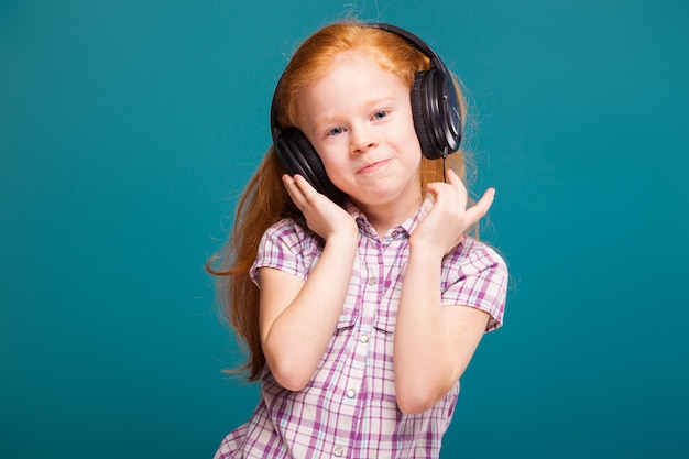 Beautiful, cute little girl in checkered shirt and earphones with long red hair listen to musik