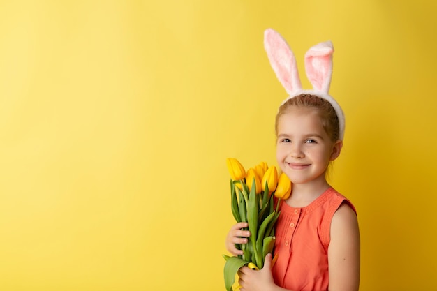 Beautiful cute little girl in Easter bunny ears smiling and holds spring bouquet of tulips