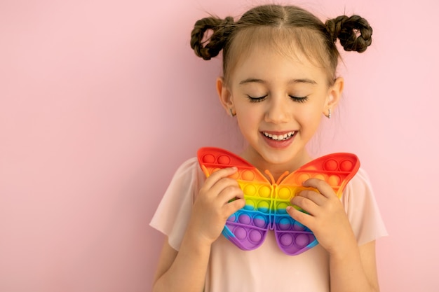 A beautiful cute little girl with her eyes closed holds a butterflyshaped popit toy in her hand