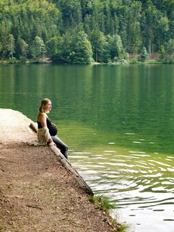 아름 다운 귀여운 임산부는 해안에 숲에서 산 호수 근처에 앉아