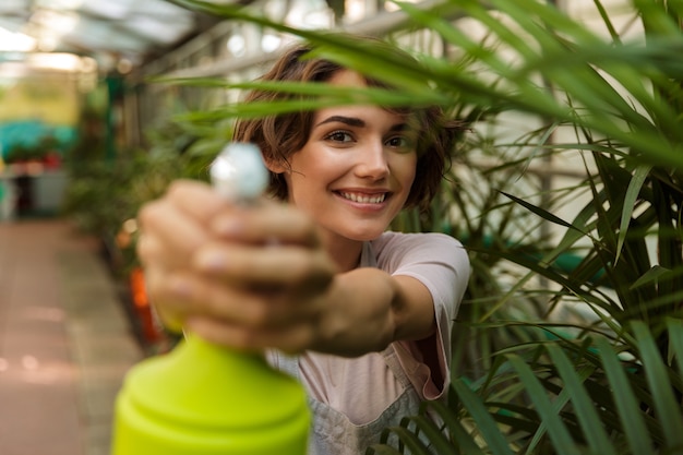 温室の植物の上に立っている美しいかわいい女性の庭師