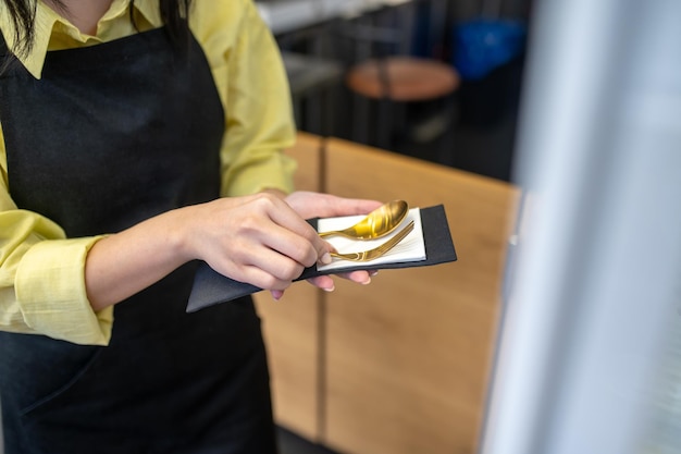 Photo beautiful cutlery. graceful female hands gently touching holding cutlery wrapped in napkin indoors without face