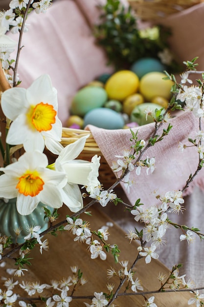 Beautiful daffodils on background of stylish natural dyed easter eggs with spring flowers on linen napkin in wicker basket Rustic Easter still life Happy Easter