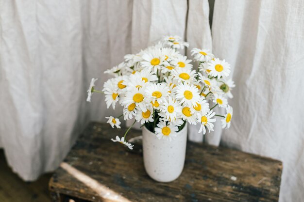 Photo beautiful daisy flowers on wooden rural chair in rustic room summer vibes simple home decor in countryside daisy bouquet in modern ceramic vase in sunny room copy space