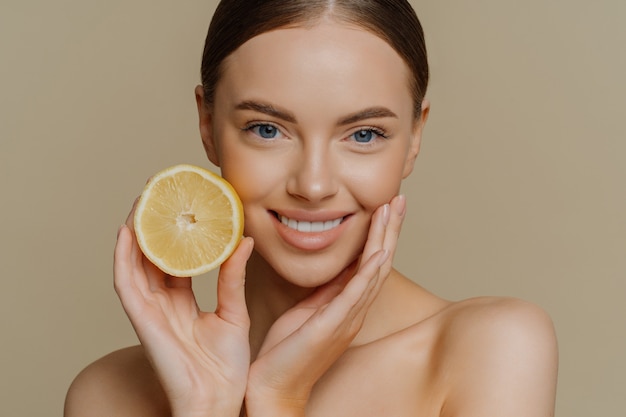 Beautiful dark haired gentle woman smiles pleasantly poses with half of lemon for skin and body care