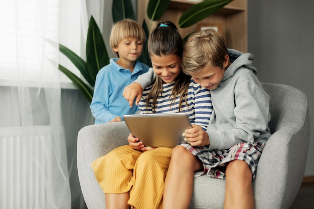 Photo the beautiful dark-haired sister and her brothers are sitting at home on the couch playing games