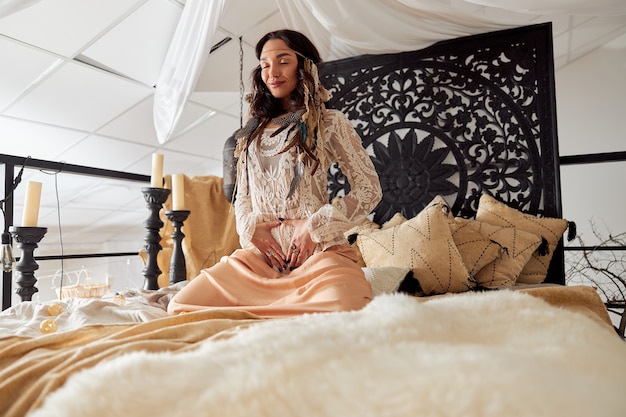 Beautiful dark haired woman in shamanic ethnic outfit in bali style decorated room