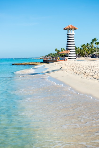 Beautiful day at sea. White sand, tropical palm trees and lighthouse on sandy shore