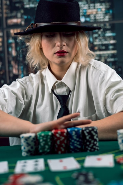 Beautiful dealer girl in a hat in a shirt and tie at the poker table follows the process